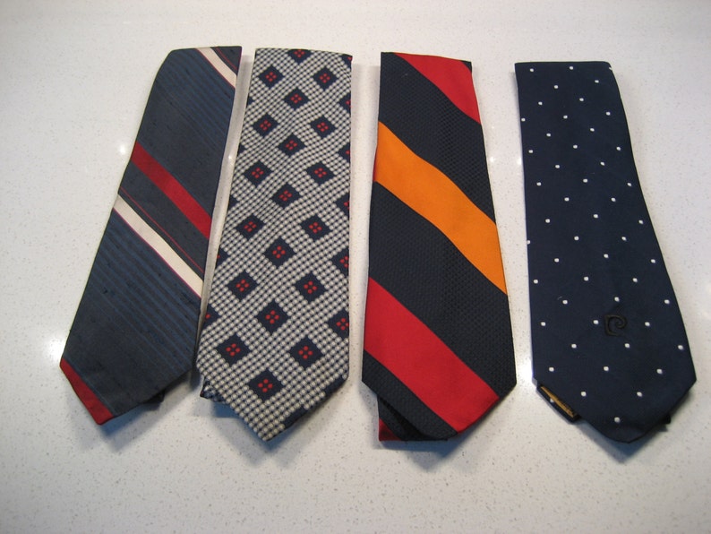 May include: Four neckties in different patterns. The ties are all navy blue with white, red, and orange accents. The patterns include stripes, polka dots, and geometric shapes.