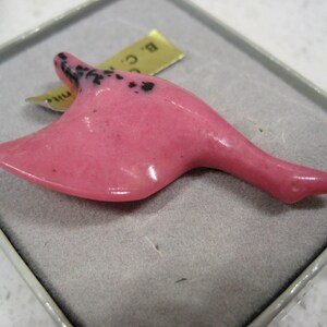 May include: A pink carved goose figurine with black speckles. The figurine is in a small white box with a gold label that reads "B.C. Mini".