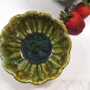 May include: A green and blue ceramic bowl with a ruffled edge. The bowl is shaped like a flower and has a deep centre.