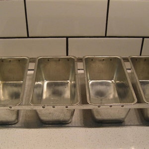 Könnte beinhalten: Eine silberne Metall-Laibform mit vier einzelnen Fächern zum Backen von Brot.