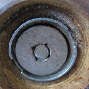K&ouml;nnte beinhalten: Nahaufnahme des Bodens einer h&ouml;lzernen Pfefferm&uuml;hle. Die M&uuml;hle hat einen Mahlmechanismus aus Metall mit einem kleinen Loch in der Mitte.