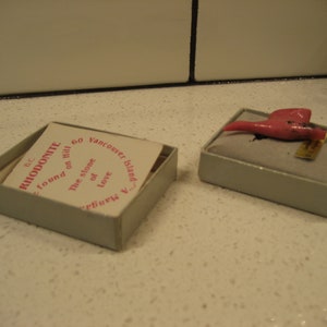May include: A small pink stone, labeled "Rhodonite", found on "the stone of love" on Galiano Island, BC. The stone is in a small, white box with a label that reads "60 Vancouver Island".