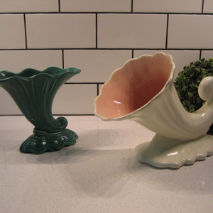 May include: Two vintage ceramic cornucopia vases. One is green with a scalloped rim and the other is white with a pink interior.