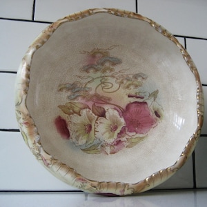 Puede incluir: Un tazón grande de cerámica blanca con un borde festoneado y un diseño floral. El tazón tiene un borde dorado y presenta flores rosas, amarillas y verdes.