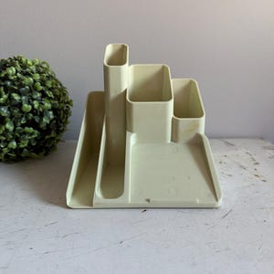 May include: A beige plastic desk organizer with multiple compartments for pens, pencils, and other office supplies.