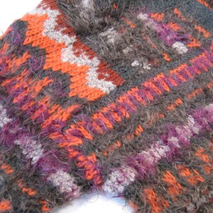 May include: Close-up of a fuzzy, multi-colored knitted fabric with a geometric pattern in shades of orange, purple, gray, and white.