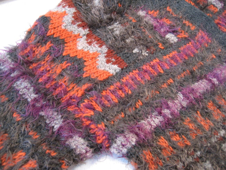 May include: Close-up of a fuzzy, multi-colored knitted fabric with a geometric pattern in shades of orange, purple, gray, and white.