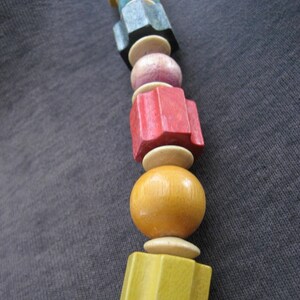 May include: A colorful wooden bead necklace with a variety of shapes and sizes. The beads are made of wood and painted in different colors, including red, yellow, blue, and green.