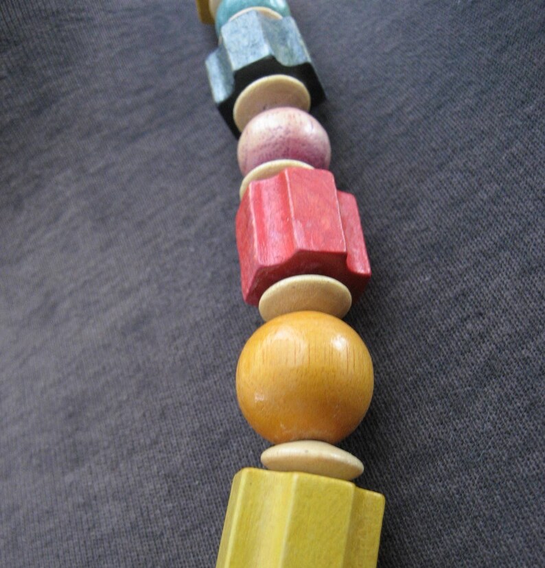 May include: A colorful wooden bead necklace with a variety of shapes and sizes. The beads are made of wood and painted in different colors, including red, yellow, blue, and green.