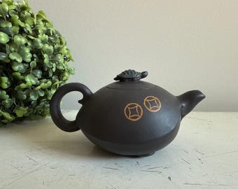 以下が含まれることがあります： 白い表面に置かれた、暗い茶色の茶器。蓋は亀の形をしていて、側面には金色の模様が2つある。