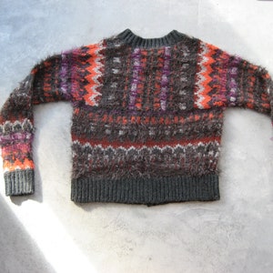 May include: A fuzzy, brown, orange, and purple sweater with a fair isle pattern. The sweater has a crew neck and long sleeves.