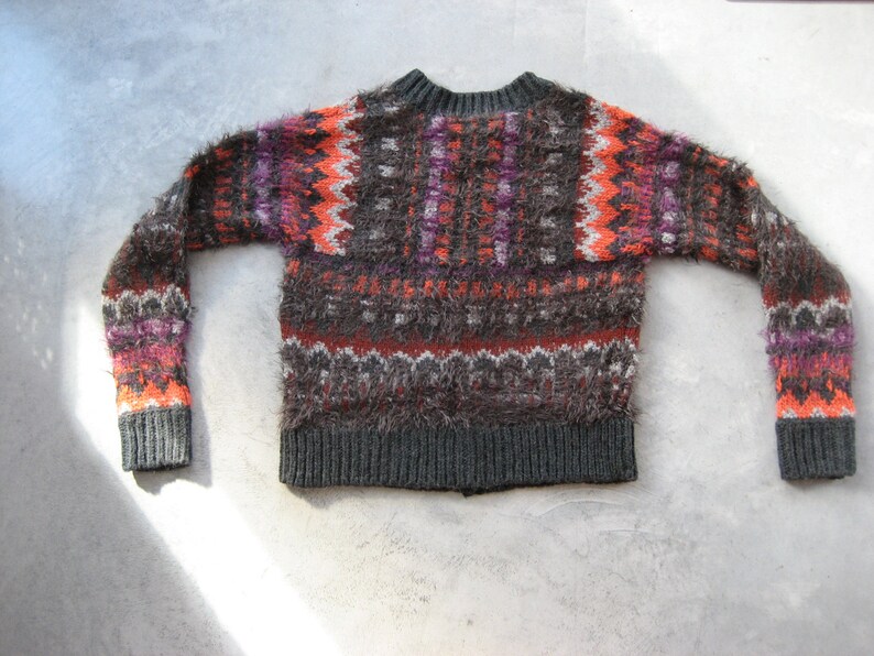 May include: A fuzzy, brown, orange, and purple sweater with a fair isle pattern. The sweater has a crew neck and long sleeves.