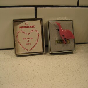 May include: A pink rhodonite bird figurine in a small box. The box has a label that reads "B.C. Rhodonite found on Hill 60 Vancouver Island. Manganese Silicate. The stone of Love."