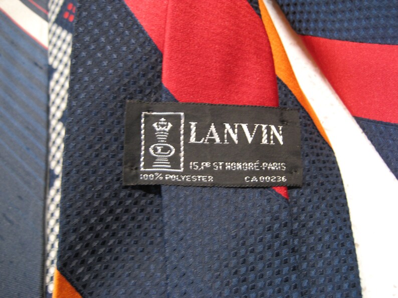 May include: A navy blue, red, white, and orange striped tie with a black label that reads "LANVIN 15, rue St. Honor&eacute; Paris 100% POLYESTER CA 00236"