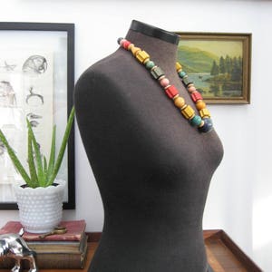 May include: A black fabric mannequin torso with a colorful wooden bead necklace. The necklace has red, yellow, green, blue, and pink beads.