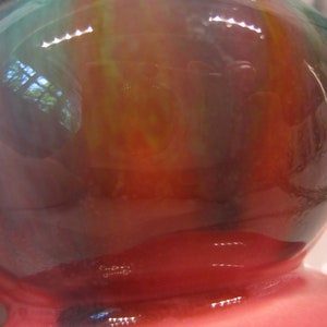May include: A round, iridescent glass vase with a pink base. The vase has a swirling pattern of green, blue, and red.