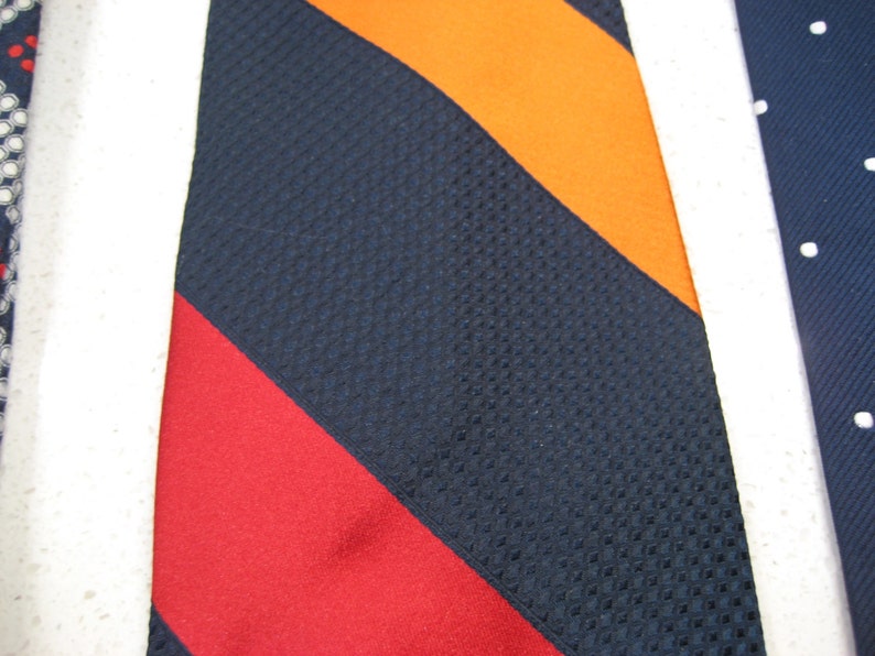 May include: A navy blue tie with orange, red, and white stripes. The tie has a textured pattern.