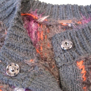 May include: A gray, fuzzy cardigan with a colorful pattern of orange, pink, and white. The cardigan has a button closure and a label that reads "Madewell".
