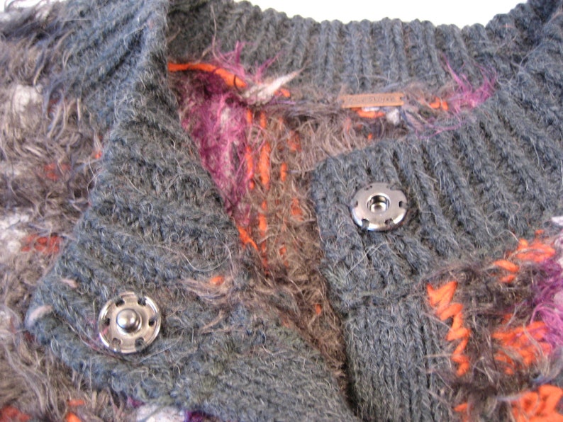 May include: A gray, fuzzy cardigan with a colorful pattern of orange, pink, and white. The cardigan has a button closure and a label that reads "Madewell".