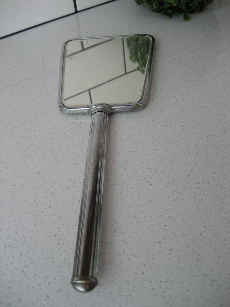 May include: A silver handheld mirror with a rectangular frame and a long, slender handle.