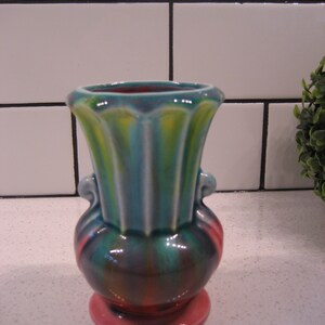 May include: A small, colourful ceramic vase with a pink base, green and yellow body, and a fluted rim. The vase has two handles on the sides.