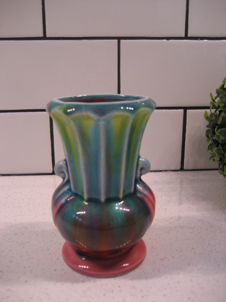 May include: A small, colourful ceramic vase with a pink base, green and yellow body, and a fluted rim. The vase has two handles on the sides.