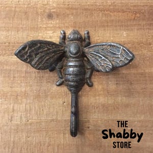 May include: A cast iron bee-shaped decorative key with detailed wings and body. The key has a dark, aged finish, and a long handle. The text "THE Shabby STORE" is printed at the bottom of the image.