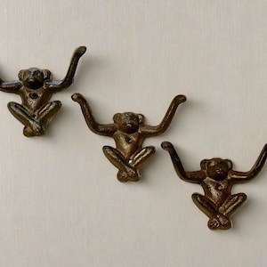 Può includere: Tre ganci in metallo a forma di scimmia in posizione seduta. I ganci sono di colore bronzo scuro e hanno una finitura rustica.