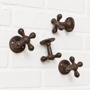 May include: Four wall-mounted hooks made of dark brown, textured cast iron. Each hook features a cross-shaped handle design with rounded ends and a circular base plate with two screw holes for mounting, resembling vintage water faucet handles.