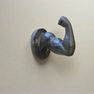 May include: A black metal wall hook shaped like a bicep, with a round base.
