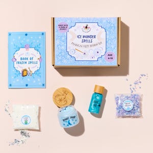 May include: A flat lay of a children's ice-themed potion kit. The kit includes a box, a book, a jar of cream, a bottle of mist, a bag of crystals, and a wooden lid. The box reads "Ice Wonder Spells" and "Magical Izzy Potion Kit".