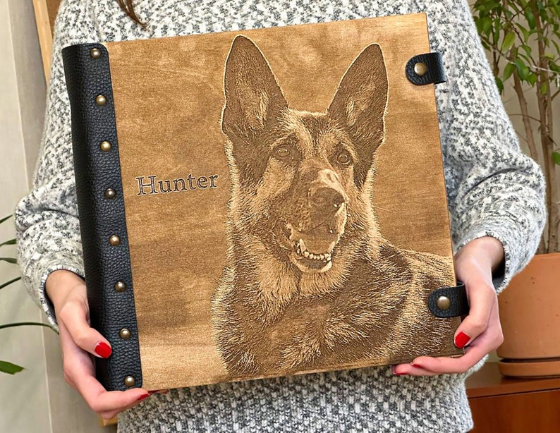 Puede incluir: Un &aacute;lbum de fotos de madera con una cubierta de cuero negro y detalles met&aacute;licos. El &aacute;lbum presenta una imagen grabada con l&aacute;ser de un pastor alem&aacute;n con el nombre "Hunter" grabado en la parte delantera.