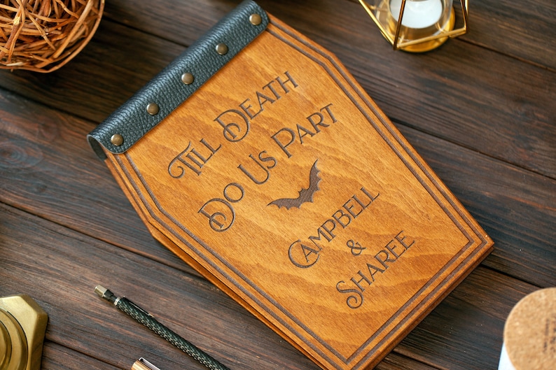 Puede incluir: Una caja de madera con forma de ata&uacute;d con una solapa de cuero negro y remaches met&aacute;licos. La caja est&aacute; grabada con el texto "Till Death Do Us Part" y una silueta de murci&eacute;lago. Los nombres "Campbell & Sharee" tambi&eacute;n est&aacute;n grabados en la caja.