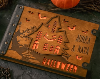 May include: Wooden Halloween-themed book featuring a haunted house design, bats, and the word "HALLOWEEN". The book is engraved with the names "AUREA & NATA". The cover is made of wood with a dark leather spine.