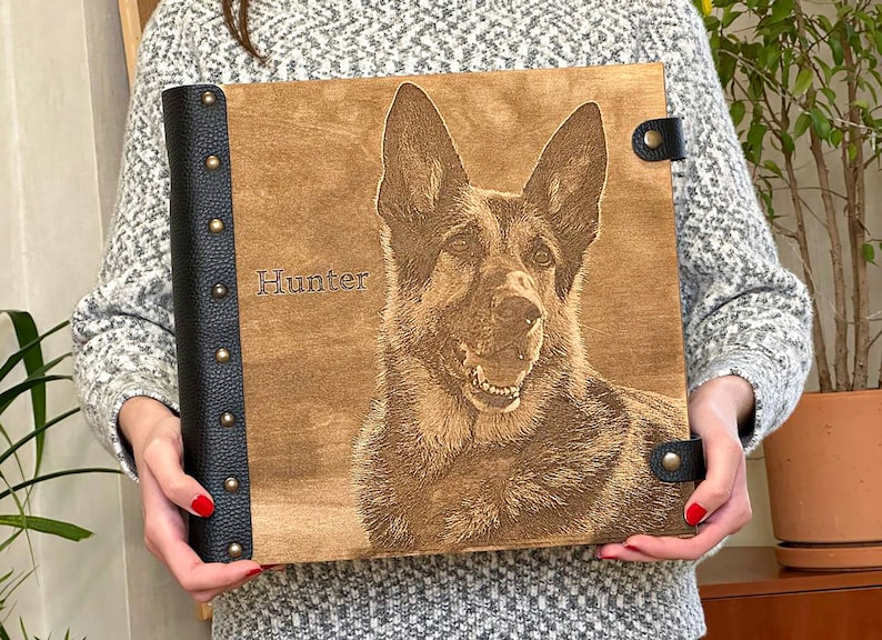 Puede incluir: Un &aacute;lbum de fotos de madera marr&oacute;n con una encuadernaci&oacute;n de cuero negro y detalles met&aacute;licos. El &aacute;lbum presenta una imagen grabada con l&aacute;ser de un pastor alem&aacute;n con el nombre "Hunter" grabado en la parte delantera.