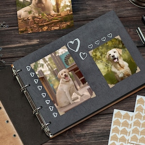 Puede incluir: Un &aacute;lbum de fotos negro con una cubierta de madera y encuadernaci&oacute;n en espiral. El &aacute;lbum tiene dos p&aacute;ginas abiertas, cada una con una foto de un perro golden retriever. El &aacute;lbum tiene un dise&ntilde;o de coraz&oacute;n decorativo en la portada.