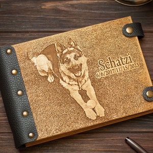 Puede incluir: Un &aacute;lbum de fotos de cuero marr&oacute;n con un borde de cuero negro y tachuelas de lat&oacute;n. La portada presenta una imagen grabada con l&aacute;ser de un perro pastor alem&aacute;n jugando con una pelota. El texto "Schatzi 6/6/2017-11/15/2023" tambi&eacute;n est&aacute; grabado en la portada.