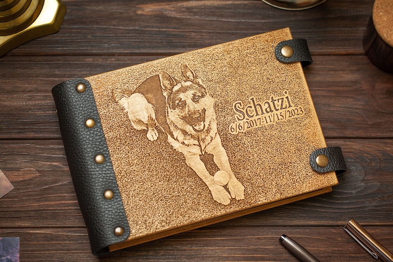 Puede incluir: Un &aacute;lbum de fotos de cuero marr&oacute;n con un borde de cuero negro y tachuelas de lat&oacute;n. La portada presenta una imagen grabada con l&aacute;ser de un perro pastor alem&aacute;n jugando con una pelota. El texto "Schatzi 6/6/2017-11/15/2023" tambi&eacute;n est&aacute; grabado en la portada.