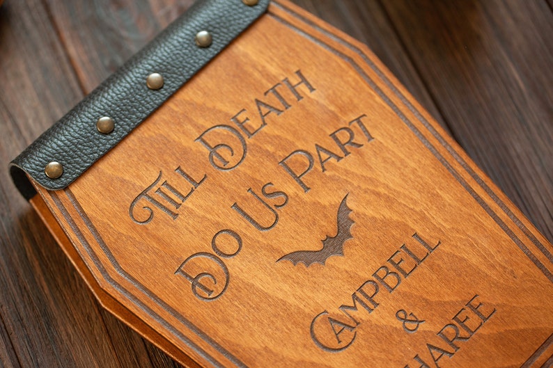 Puede incluir: Un letrero de madera con forma de ata&uacute;d con el texto "Till Death Do Us Part" y un gr&aacute;fico de murci&eacute;lago. El letrero est&aacute; personalizado con los nombres "Campbell & JaRee".
