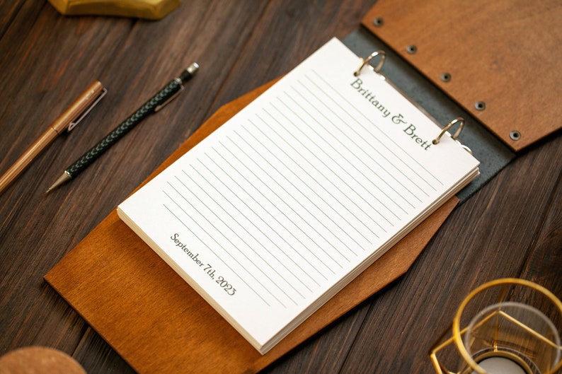 Puede incluir: Un libro de visitas encuadernado en cuero marr&oacute;n con un anillo de encuadernaci&oacute;n. La portada est&aacute; grabada con el texto "Brittany & Brett" y la fecha "September 7th, 2023".