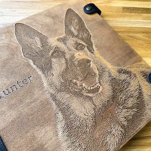 Puede incluir: Un &aacute;lbum de fotos de cuero marr&oacute;n con una correa negra y una imagen grabada con l&aacute;ser de un perro pastor alem&aacute;n con el nombre "Hunter" en la parte delantera.