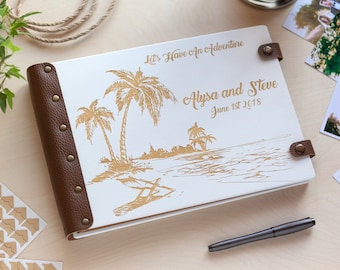 Könnte beinhalten: Weißes, ledergebundenes Fotoalbum mit einem goldgeprägten Design von Palmen und einer Strandszene. Das Album trägt den Text "Let's Have An Adventure" und "Alyssa and Steve June 1st 2018" auf dem vorderen Umschlag.