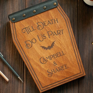 Puede incluir: Una caja de madera con forma de ata&uacute;d con una tapa de cuero negro y detalles met&aacute;licos. La caja est&aacute; grabada con el texto "Till Death Do Us Part" y los nombres "Campbell & Sharee".