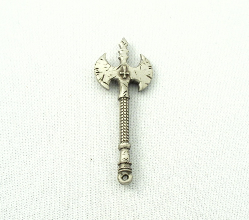 May include: A silver-toned axe pendant with a cross design on the blade. The axe has a detailed, textured surface and a pointed tip.