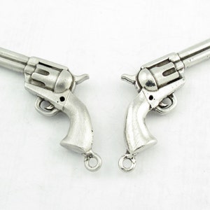 May include: Two silver-toned metal charms shaped like revolvers. Each charm has a ring attached to the bottom for attaching to a necklace or bracelet.
