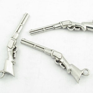 May include: Three silver-toned rifle charms with a loop for attaching to a necklace or bracelet.