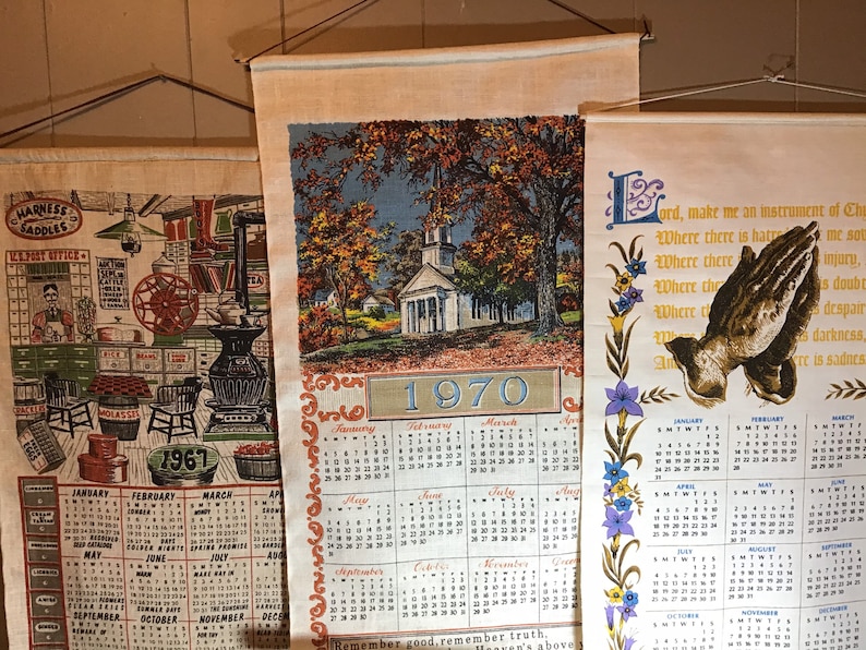 May include: Three vintage wall calendars with a white background and colorful illustrations. The top calendar features a church with a white steeple and a blue sky. The middle calendar features a black and white illustration of a blacksmith shop. The bottom calendar features a prayer with a dove and the text "Lord, make me an instrument of Thy peace."