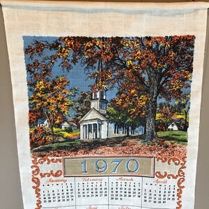 May include: A vintage linen tea towel with a colorful illustration of a church and trees in autumn. The towel features a calendar for the year 1970 with the months of January, February, March, and April.