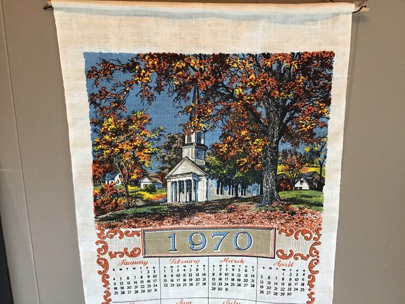 May include: A vintage linen tea towel with a colorful illustration of a church and trees in autumn. The towel features a calendar for the year 1970 with the months of January, February, March, and April.