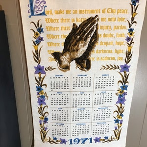 May include: A vintage kitchen towel with a floral border and a calendar for the year 1971. The towel features a prayer in a decorative font and an image of praying hands.